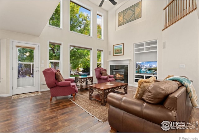 living area with a ceiling fan, built in features, wood finished floors, a high end fireplace, and baseboards