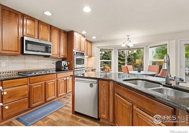 kitchen with dark stone counters, brown cabinetry, a notable chandelier, stainless steel appliances, and a sink