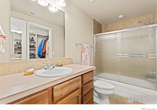 bathroom with tile patterned floors, visible vents, toilet, vanity, and a textured wall