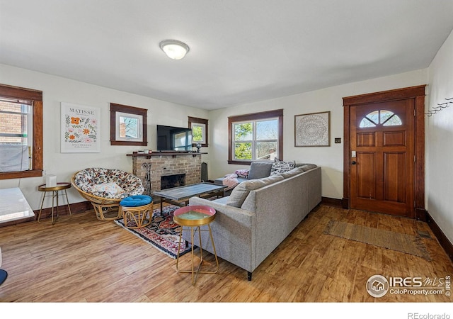 living room featuring a brick fireplace, baseboards, and wood finished floors