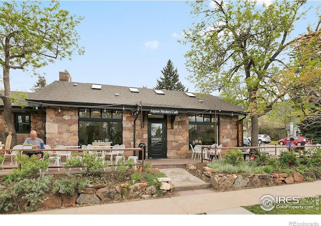 view of front of house featuring stone siding, a chimney, and a shingled roof