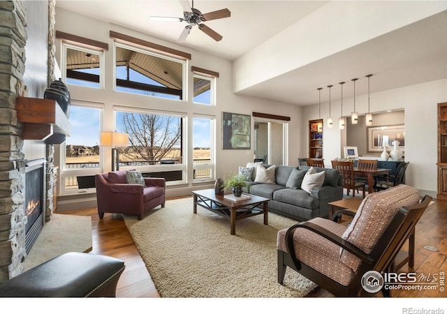 living room featuring a stone fireplace, a towering ceiling, a ceiling fan, and wood finished floors