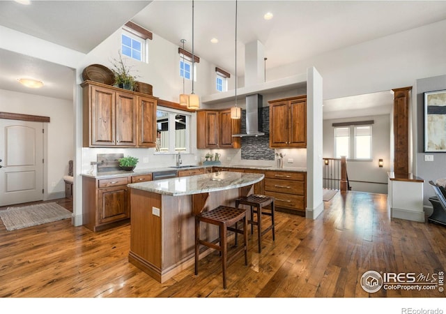 kitchen featuring brown cabinets, a sink, hardwood / wood-style floors, a center island, and wall chimney exhaust hood