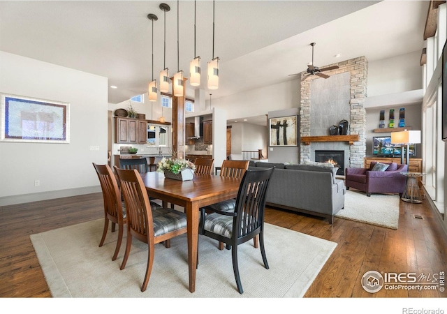 dining room with a ceiling fan, hardwood / wood-style flooring, recessed lighting, a high ceiling, and a fireplace