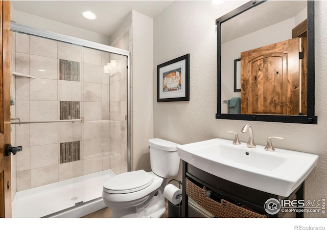 full bath with vanity, toilet, a shower stall, and a textured wall