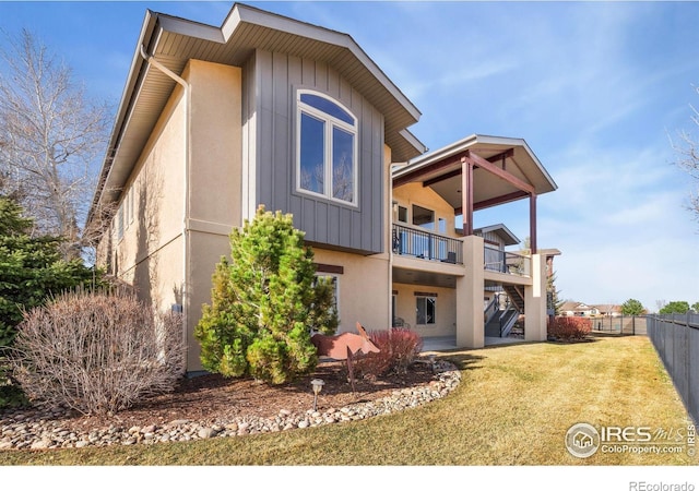 rear view of house featuring stucco siding, fence, stairway, a yard, and board and batten siding