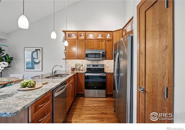 kitchen featuring a peninsula, a sink, stainless steel appliances, glass insert cabinets, and brown cabinets