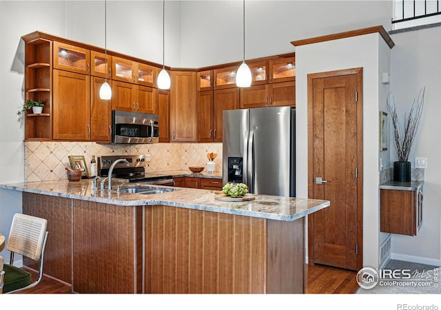 kitchen featuring light stone countertops, brown cabinets, a peninsula, appliances with stainless steel finishes, and tasteful backsplash