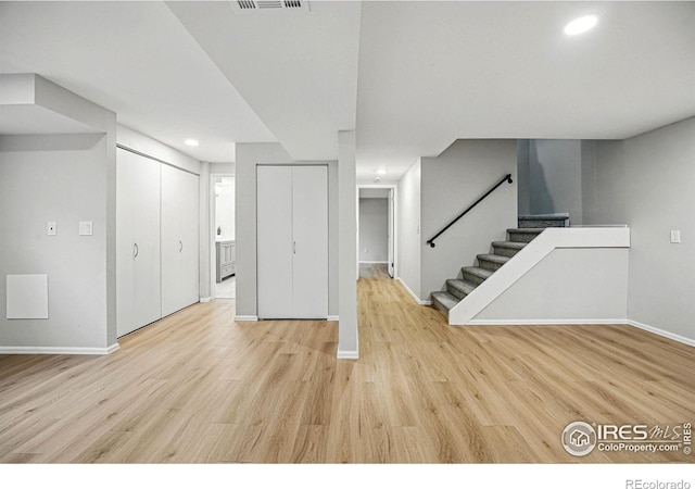 finished basement with stairway, visible vents, baseboards, and light wood-style floors