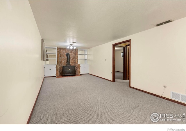 unfurnished living room featuring a wood stove, carpet, visible vents, and a textured ceiling