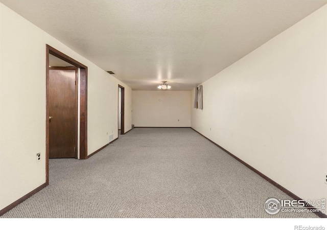 empty room with carpet flooring, baseboards, and a textured ceiling