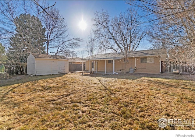 back of house with an outbuilding, fence, a yard, a storage shed, and brick siding