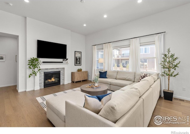 living room with visible vents, a glass covered fireplace, wood finished floors, recessed lighting, and baseboards