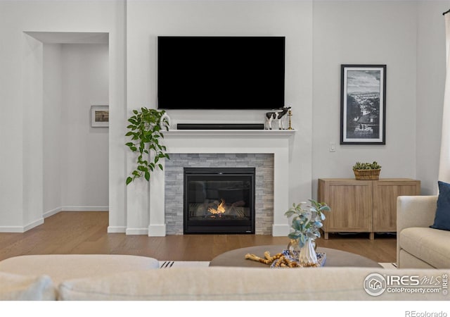 living area with a glass covered fireplace, baseboards, and wood finished floors