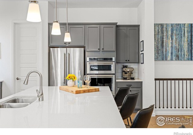 kitchen with light countertops, gray cabinets, hanging light fixtures, stainless steel appliances, and a sink