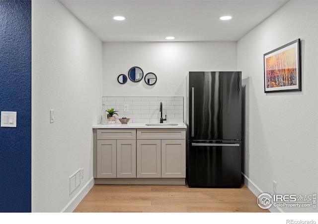 kitchen featuring light wood-type flooring, gray cabinetry, a sink, backsplash, and freestanding refrigerator