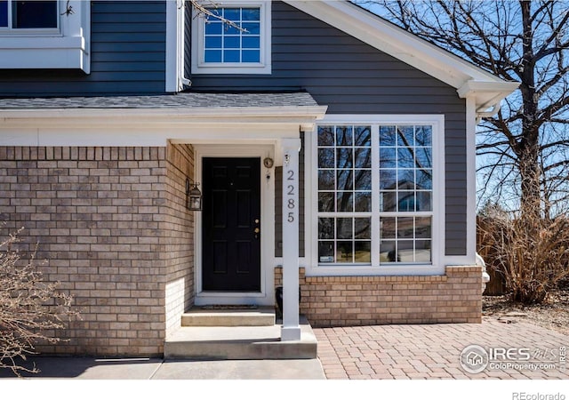 property entrance featuring brick siding and a shingled roof