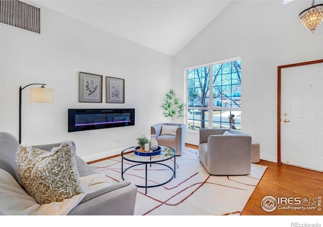 living area with visible vents, high vaulted ceiling, wood finished floors, a glass covered fireplace, and baseboards