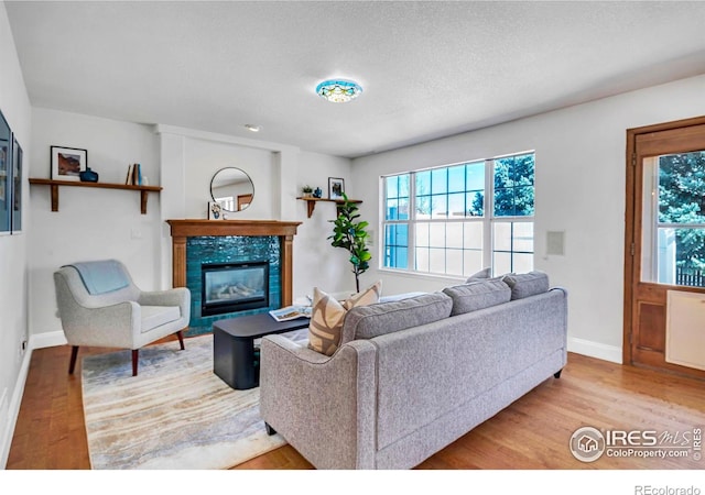 living area with a textured ceiling, wood finished floors, baseboards, and a tile fireplace