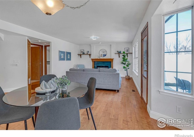 dining space featuring a fireplace, light wood-type flooring, and baseboards