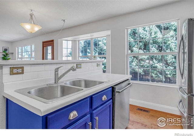 kitchen featuring light wood-type flooring, blue cabinetry, a sink, stainless steel appliances, and tasteful backsplash