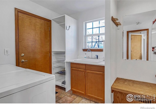 laundry area with washing machine and dryer, cabinet space, stone finish flooring, and a sink