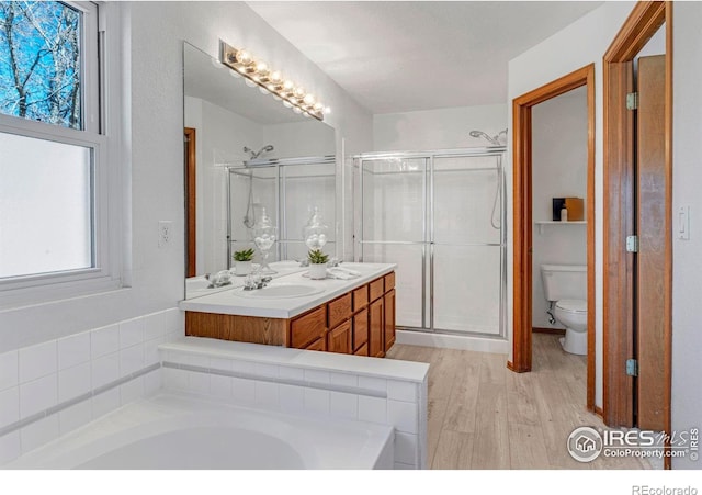 full bathroom with double vanity, a stall shower, toilet, and wood finished floors