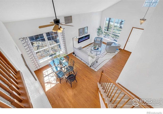 living area featuring high vaulted ceiling, a ceiling fan, a glass covered fireplace, wood finished floors, and baseboards