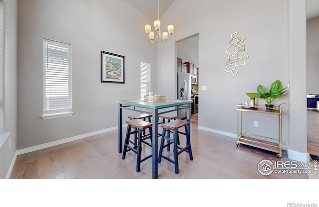 dining area with light wood-type flooring, baseboards, high vaulted ceiling, and a chandelier