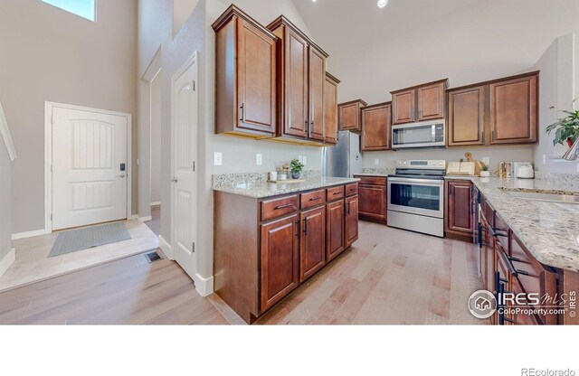 kitchen with stainless steel appliances, light wood-type flooring, a towering ceiling, and a sink