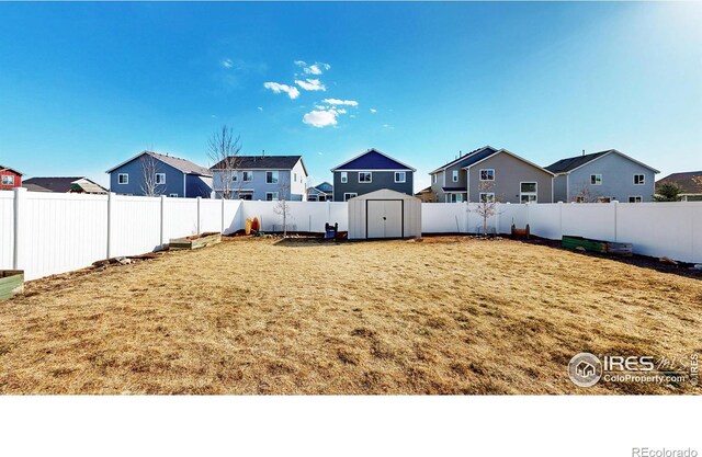 view of yard featuring an outdoor structure, a storage unit, a fenced backyard, and a residential view