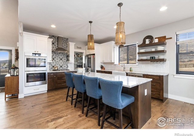 4528 Del Colina Way, Laporte, CO 80535 - kitchen with appliances with stainless steel finishes, wall chimney range hood, backsplash, white cabinets, and a center island