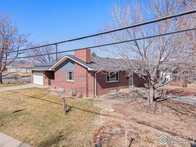 view of front of home with brick siding, solar panels, a chimney, a garage, and driveway