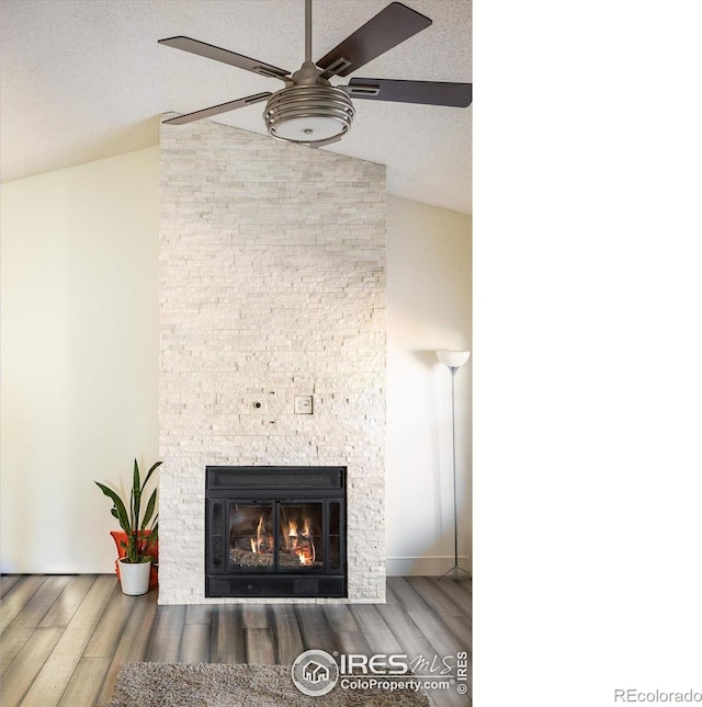 interior details featuring a stone fireplace, wood finished floors, a ceiling fan, and a textured ceiling