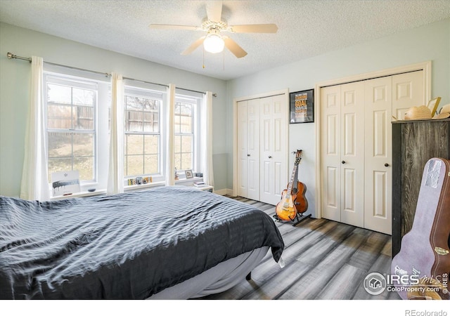 bedroom with a textured ceiling, two closets, ceiling fan, and wood finished floors