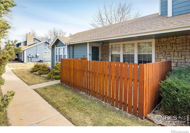 view of front of house featuring fence, stone siding, roof with shingles, and a chimney