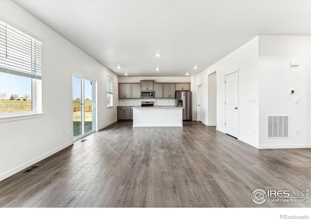 unfurnished living room with visible vents, baseboards, and dark wood-style flooring