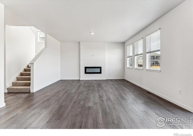 unfurnished living room featuring a glass covered fireplace, stairway, baseboards, and wood finished floors