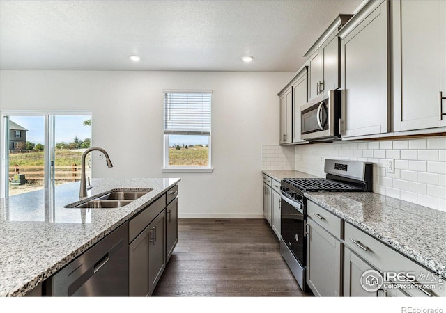 kitchen with tasteful backsplash, gray cabinets, appliances with stainless steel finishes, dark wood-style floors, and a sink