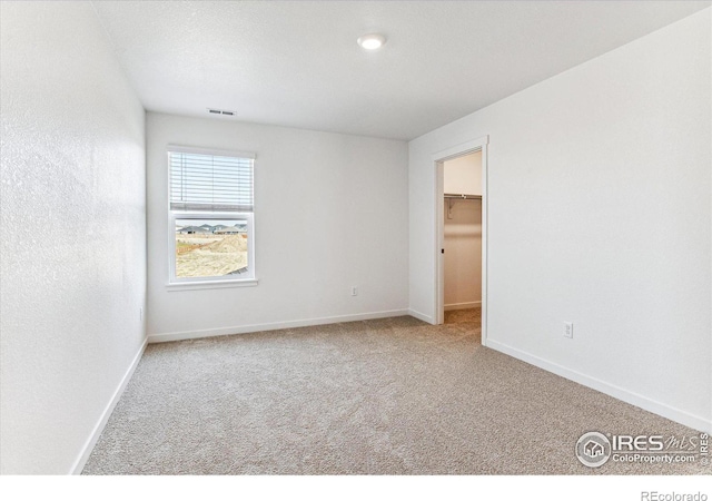 unfurnished bedroom with a spacious closet, carpet flooring, baseboards, and visible vents