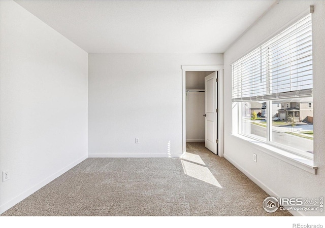 unfurnished bedroom featuring a walk in closet, baseboards, and carpet floors