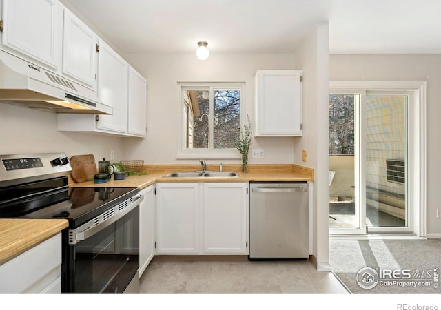 kitchen with a sink, under cabinet range hood, appliances with stainless steel finishes, white cabinets, and light countertops