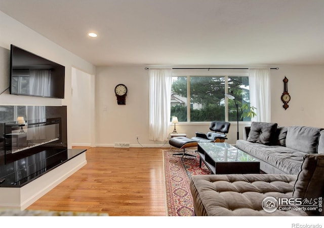 living room featuring visible vents, baseboards, recessed lighting, wood finished floors, and a glass covered fireplace