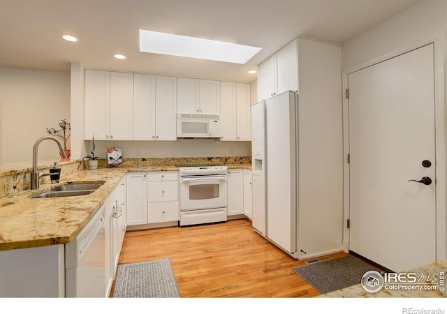 kitchen with a sink, white cabinetry, white appliances, a skylight, and light stone countertops