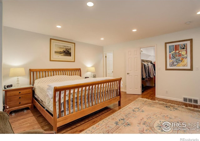 bedroom with a spacious closet, visible vents, baseboards, recessed lighting, and wood finished floors