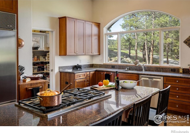 kitchen featuring a sink, dark stone countertops, brown cabinetry, and stainless steel appliances