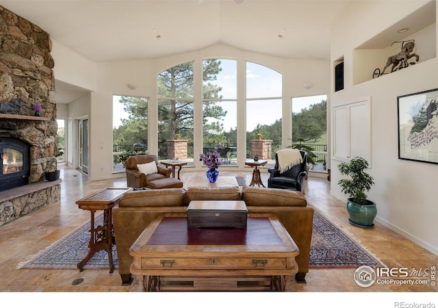 living area with a stone fireplace, high vaulted ceiling, and baseboards