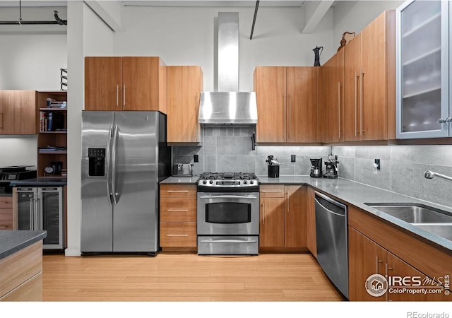 kitchen featuring brown cabinets, a sink, stainless steel appliances, wine cooler, and wall chimney exhaust hood