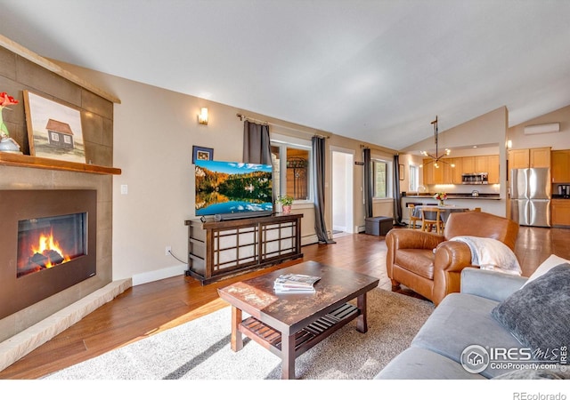 living room featuring wood finished floors, baseboards, lofted ceiling, a tile fireplace, and a notable chandelier