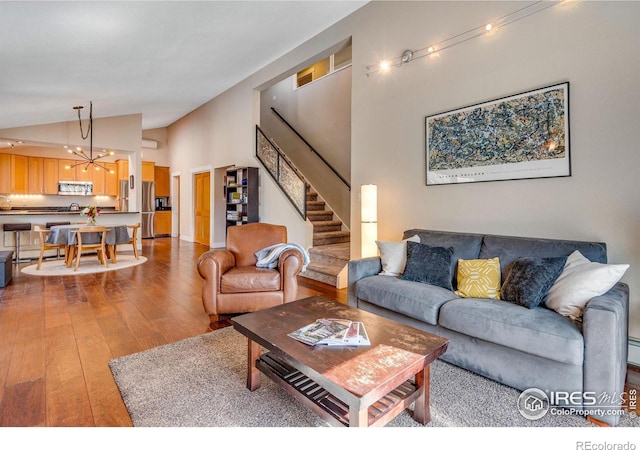 living room with a chandelier, high vaulted ceiling, stairs, and light wood-style floors